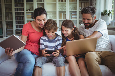 Happy family sitting on sofa and using laptop, mobile phone and digital tablet at home Happy family sitting on sofa and using laptop, mobile phone and digital tablet at home